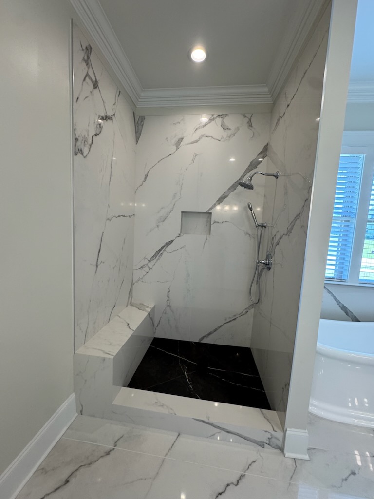 Walk-in shower with marble-look porcelain slab walls and a black stone pan in a Gulf Shores AL condo bathroom remodel