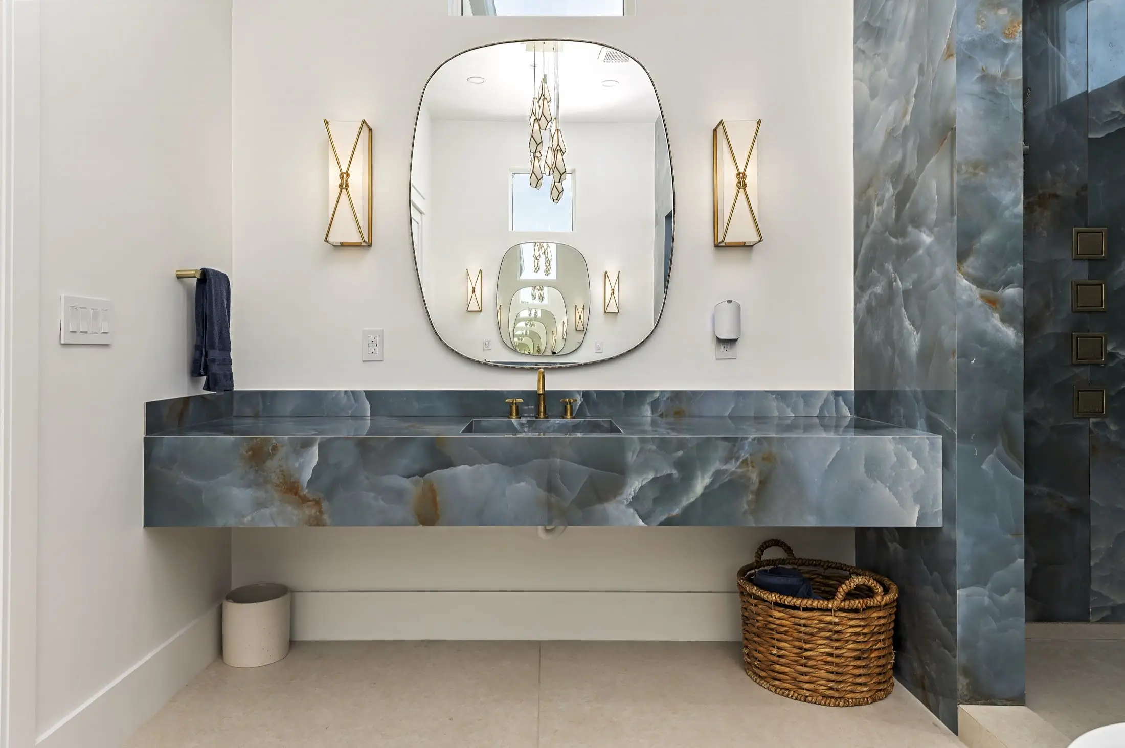 Floating blue onyx-look stone vanity with brass faucet and matching slab wall in an Orange Beach AL bathroom