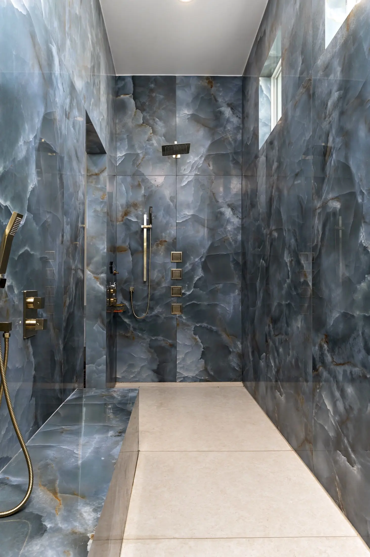 Walk-in shower finished floor to ceiling in blue onyx-look slabs with brass fixtures in Orange Beach AL
