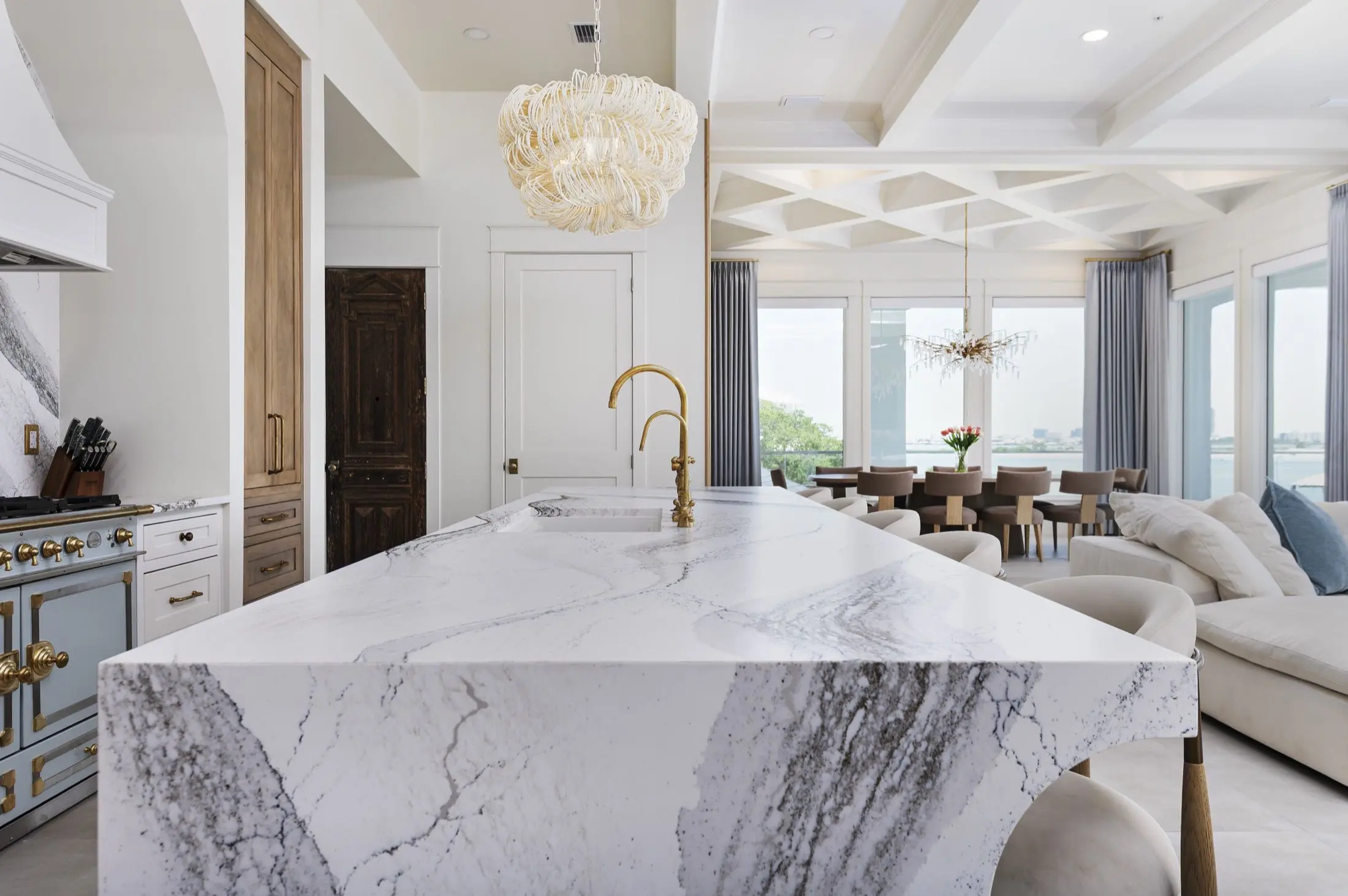 Kitchen island with veined stone waterfall countertop and brass faucets in an Orange Beach AL waterfront home
