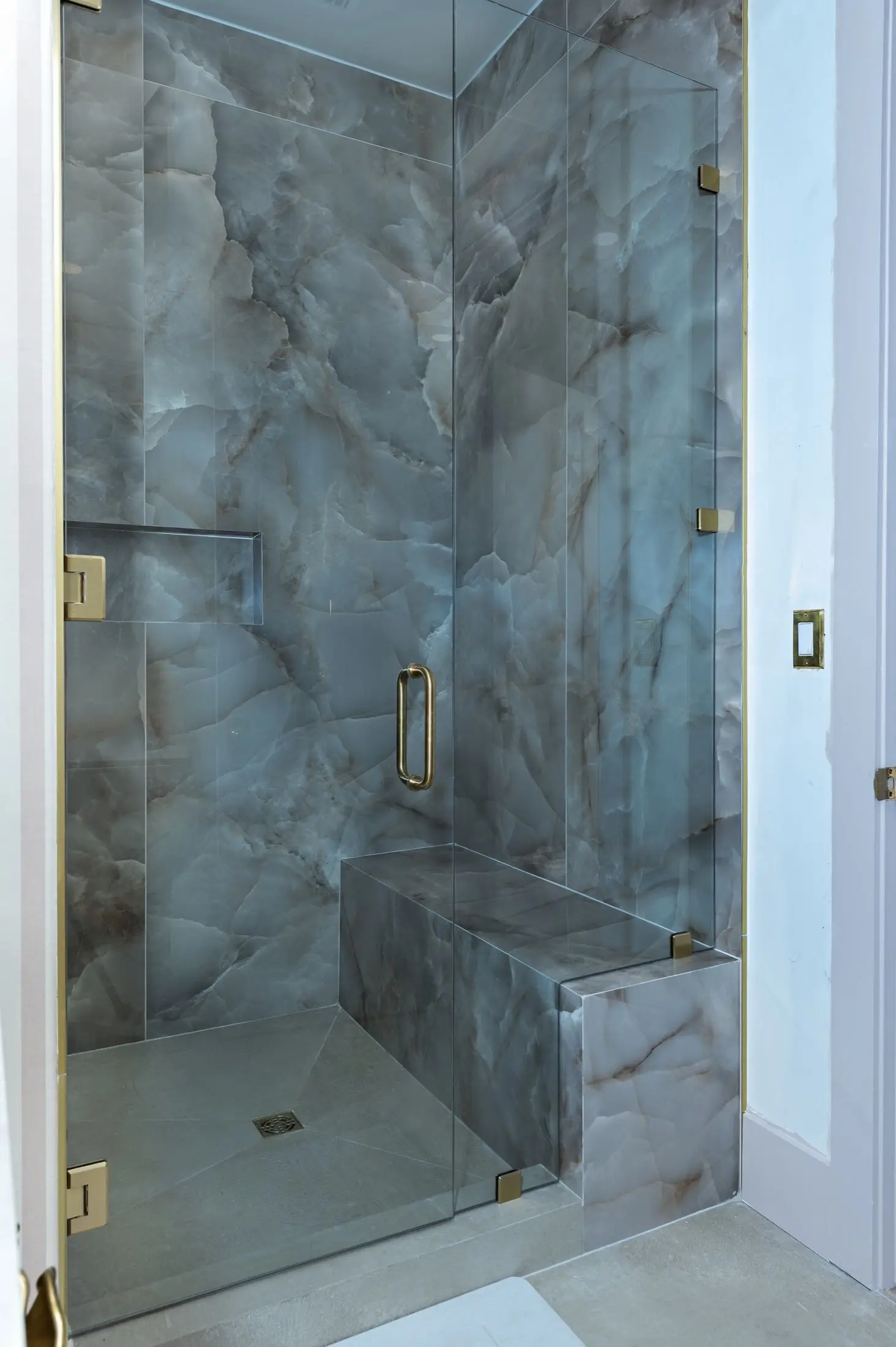 Glass-enclosed shower with smoky grey onyx-look slab walls and a stone bench