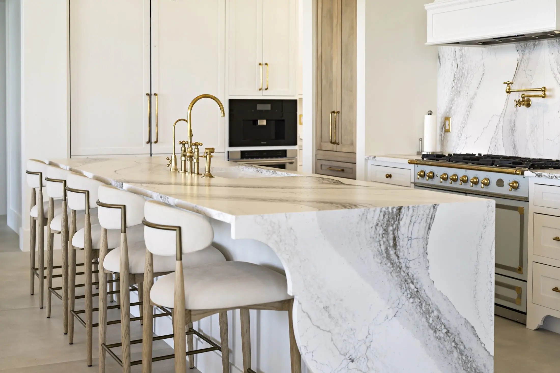 Curved stone island with waterfall edge and upholstered bar stools in a custom kitchen remodel