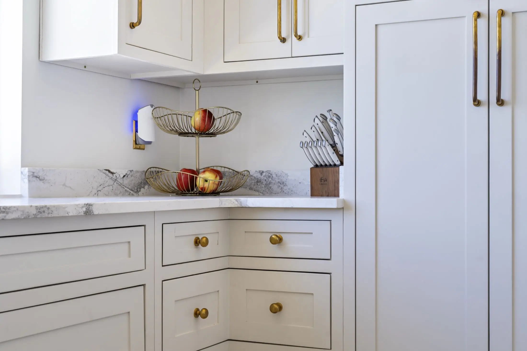 White shaker kitchen cabinets with a marble countertop and brass hardware