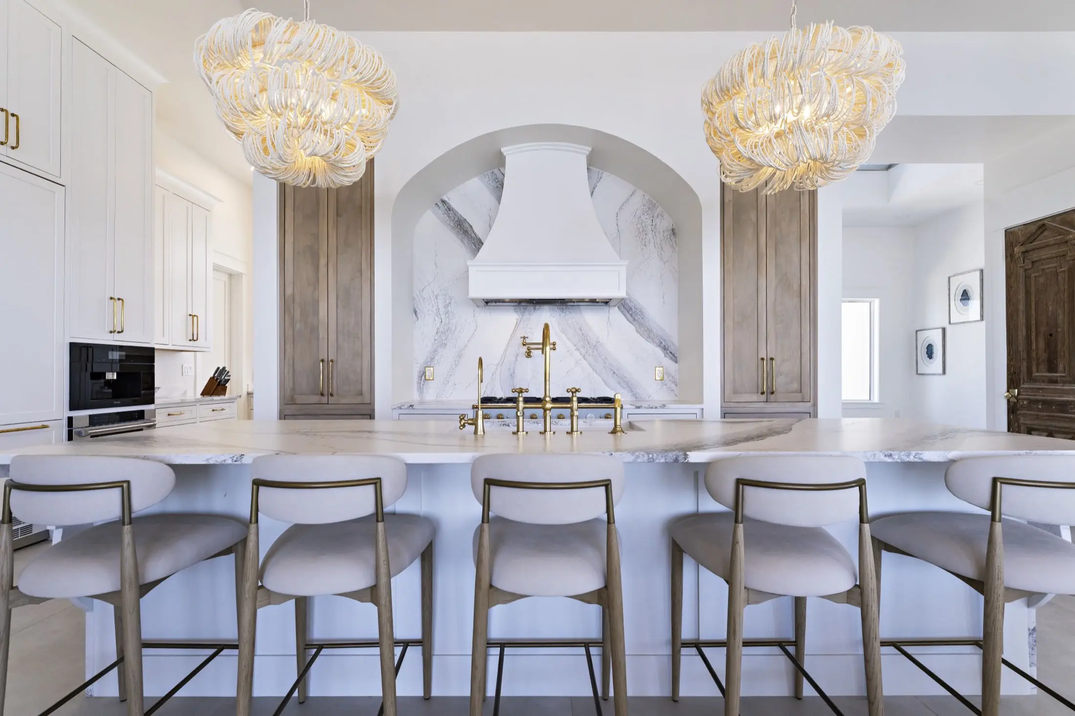 Open kitchen with a large stone island, slab range alcove and double chandeliers in an Orange Beach AL remodel