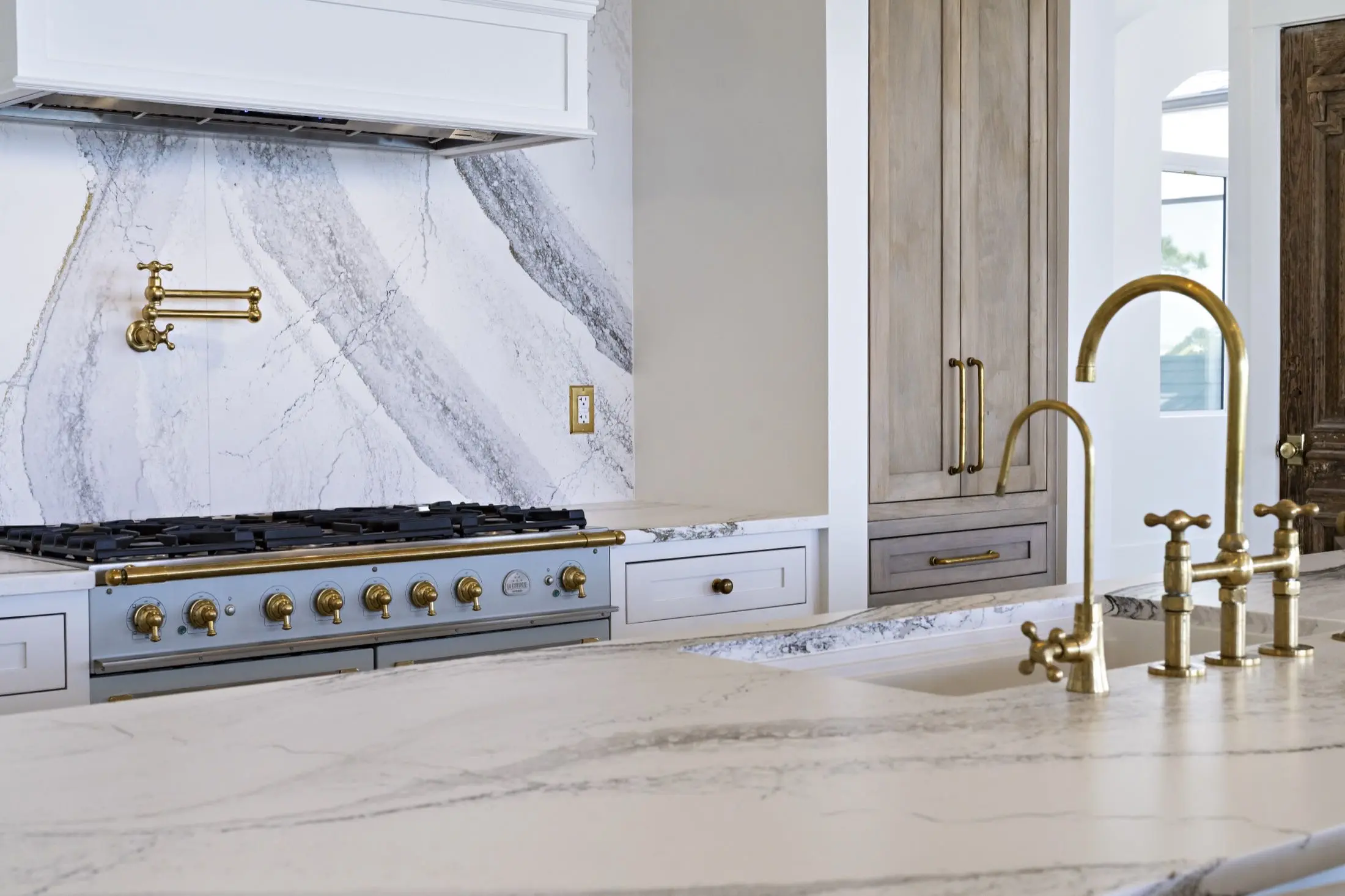 Range wall with full-height stone slab backsplash and brass pot filler in a custom kitchen