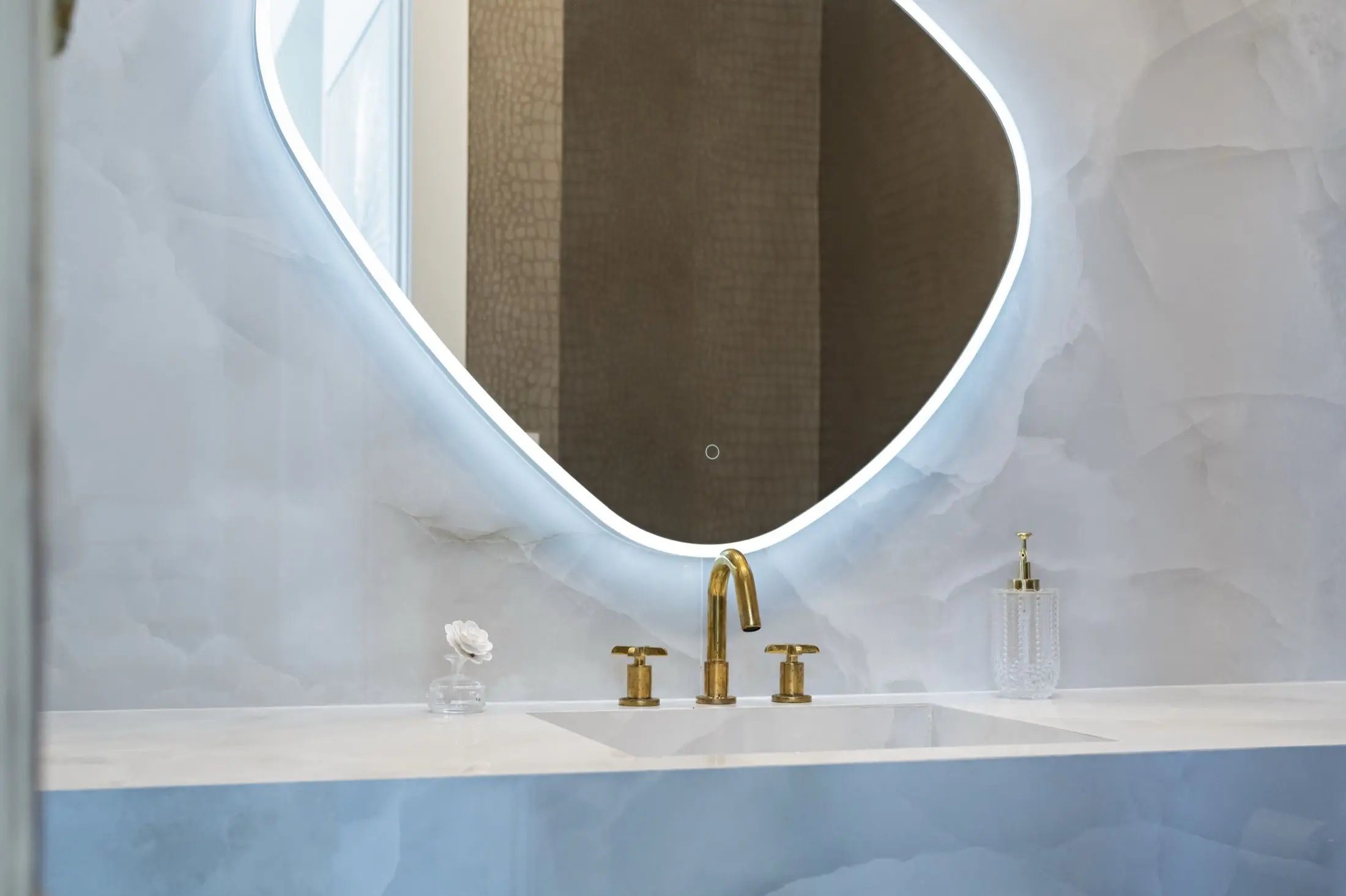 Powder bathroom with white onyx-look slab walls, sculpted LED mirror and brass faucet