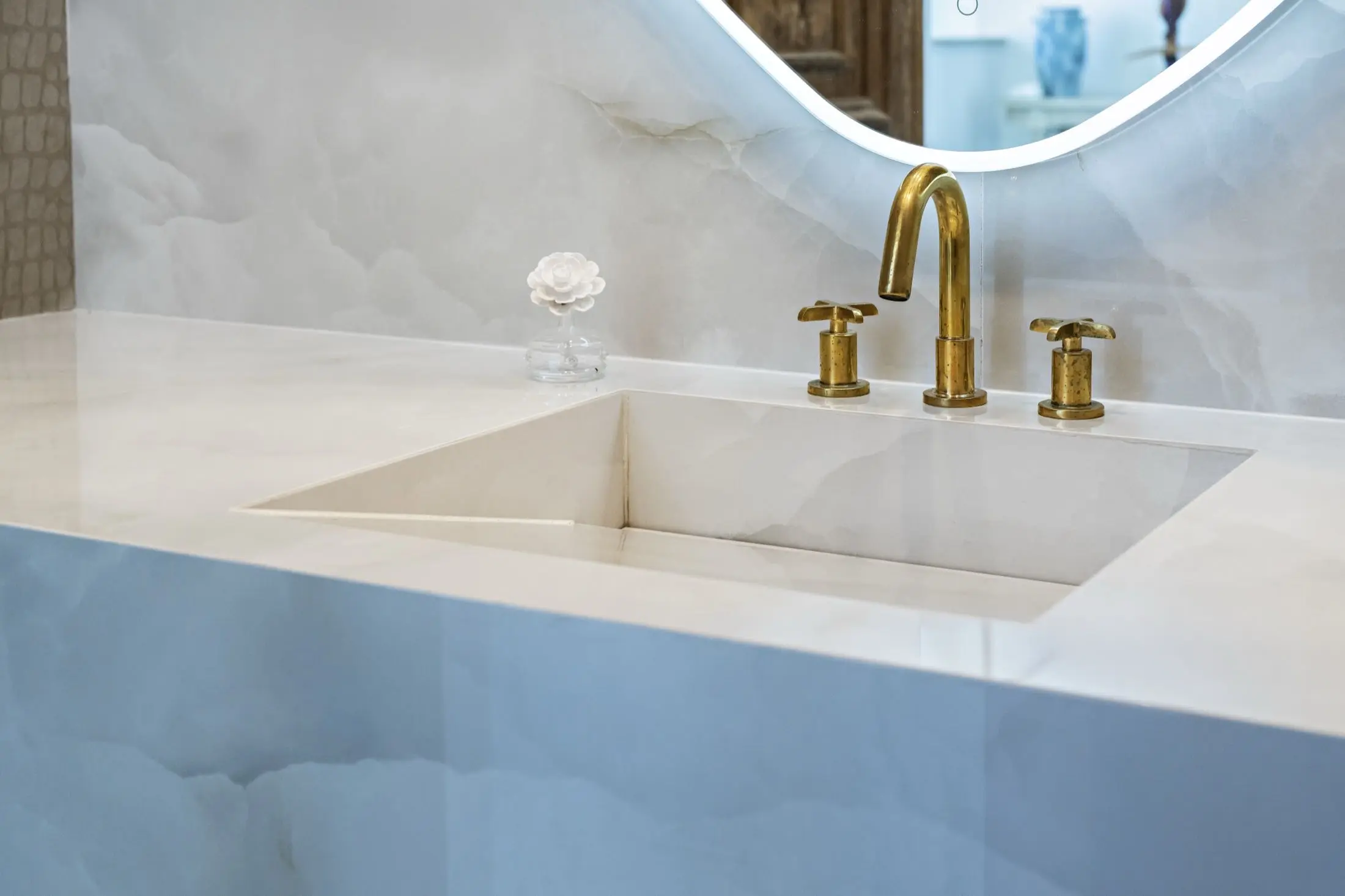 Stone vanity with integrated sink and brushed gold faucet against onyx-look slab walls